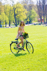 Fototapeta premium Young woman in short colorful dress with long hair rides a bicyc
