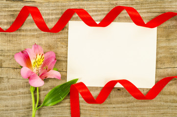 Empty card, flower and red ribbon on wooden background