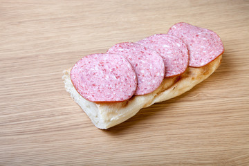 Sandwich of white bread with slices of sausage on a light wooden