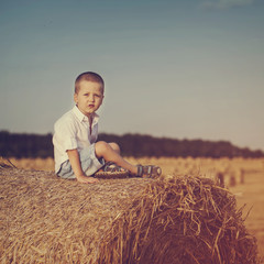 Naklejka na ściany i meble Funny little kid boy sitting on hay stackl. Active outdoors leis