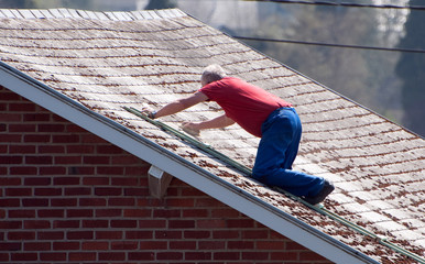 Vieil homme nettoyant son toit en ardoise sur son échelle
