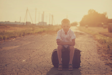 the child sits on a suitcase in the summer sunny day, the travel