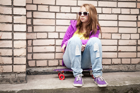 Blond teenage girl in a sunglasses with skateboard
