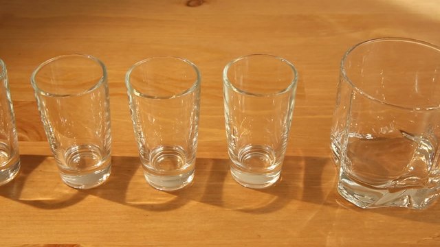 A row of small wine glasses stopping by a whiskey glass