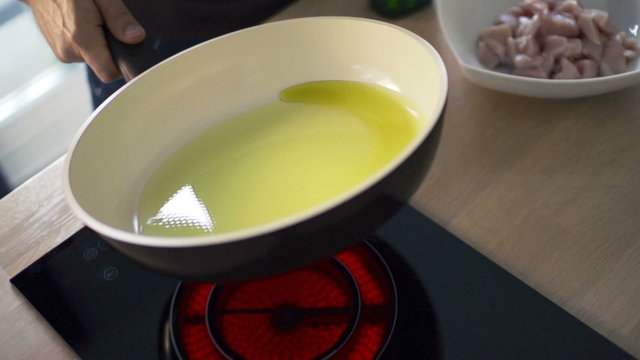 Man hand mixing olive oil on pan over induction hob in kitchen
