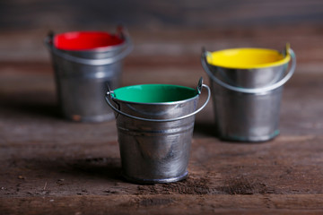Metal buckets with colorful paint on wooden background