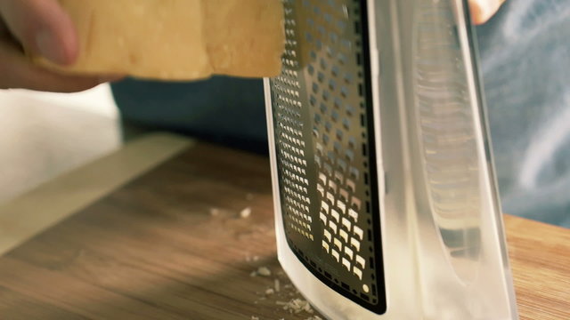Closeup of man grating cheese on grater in kitchen