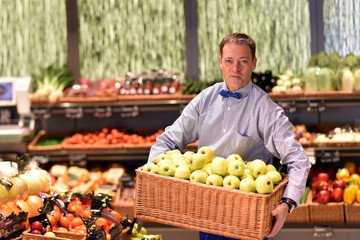 Verkäufer im supermarkt räumt Waren ein, Obststiege mit Äpfeln