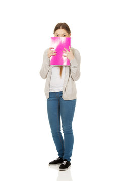 Teen woman hiding behind a notebook.