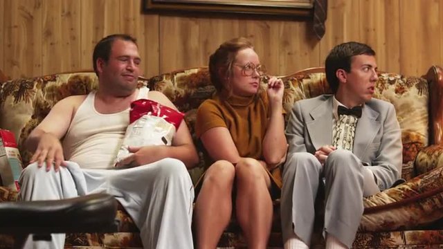 MS Overweight man eating potato chips asking woman to pull his finger while sitting on sofa, Orem, Utah, USA