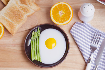 Healthy breakfast with fried egg, toasts and orange on wooden ta