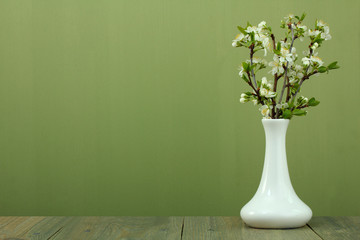Fototapeta premium branches of cherry blossoms in a vase on a wooden background
