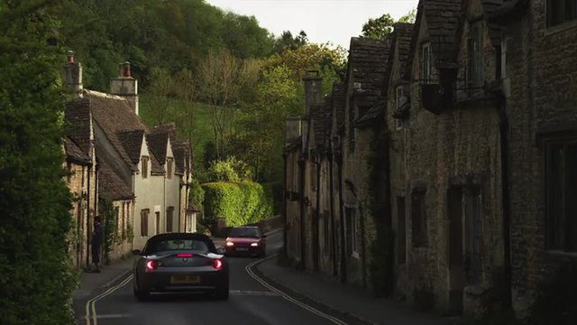 WS Two cars on village road / Castle Combe, Cotswolds, Wiltshire, UK