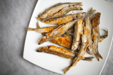 Fried smelts lays on a white plate over gray tablecloth
