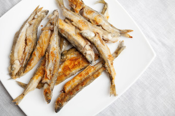 Pile of fried smelts fish lays on a white plate, closeup photo w