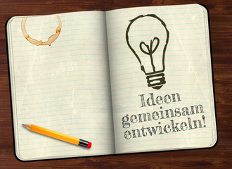 Notizbuch mit Ideen gemeinsam entwickeln und Glühbirne