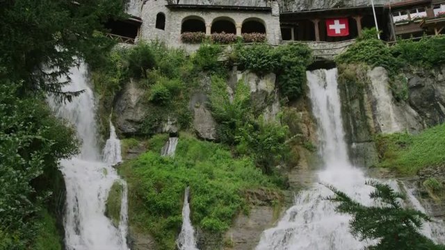 Slow motion/medium shot of waterfall and buildings on cliffs / St. Beatus Caves, Switzerland