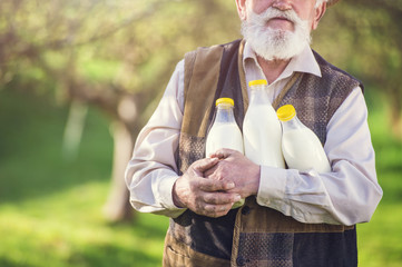 Senior farmer with milk bottles outside in green nature