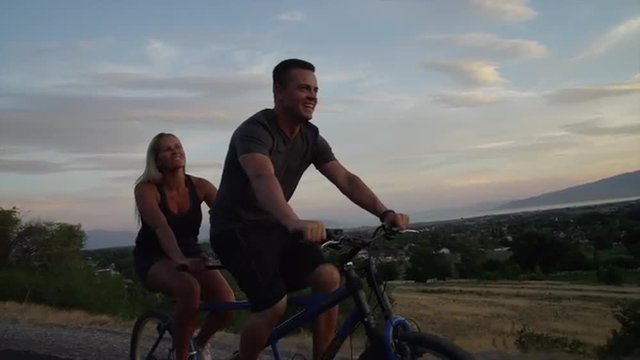 Tracking medium shot of couple riding tandem bicycle on road / Cedar Hills, Utah, United States