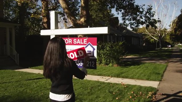 MS Woman sticking "Sold" sign in front of suburban house, Provo, Utah, USA