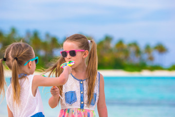 Two little girls eating bright lollipops on the beach