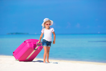 Little adorable girl with big suitcase on tropical white beach