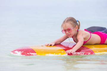 Little adorable girl on a surfboard in the turquoise sea