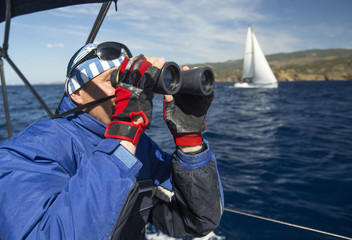 Greek skipper looks through binoculars on his yacht.