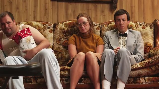 MS Overweight  man wearing pajamas, holding bag of chips sitting by nerdy couple on sofa, Orem, Utah, USA