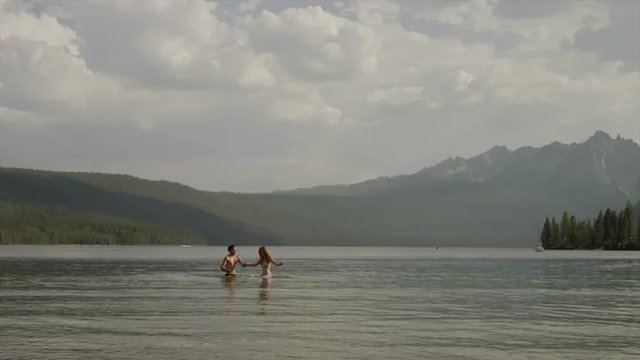 Wide shot of young couple splashing in lake / Redfish Lake, Idaho, United States