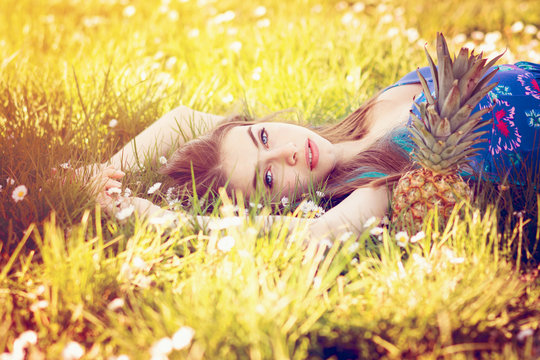 Young woman lying in grass in summer with pineapple next to her