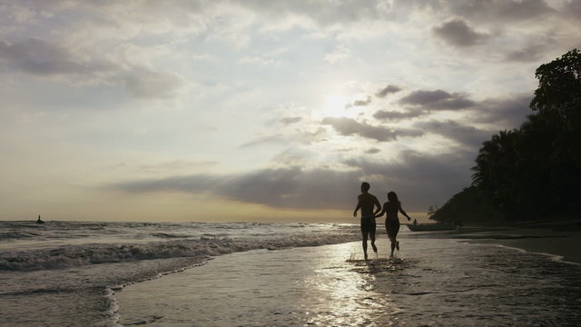 Wide panning shot of couple running on beach at sunset / Esterillos, Puntarenas, Costa Rica