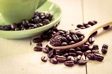 roasted coffee beans in wooden spoon on green cup background in