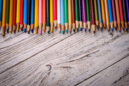 Colored pencils in a row on wooden background.