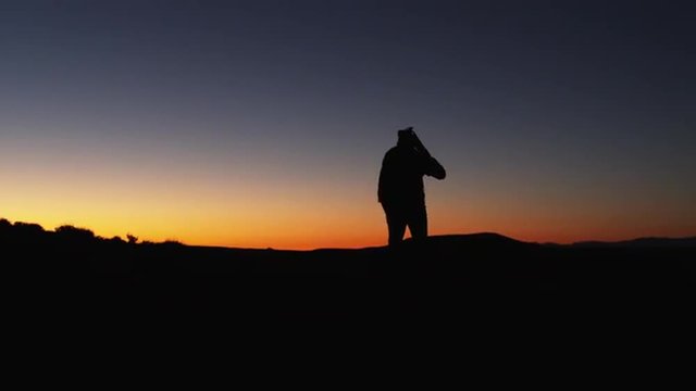WS PAN Silhouette of photographer walking, carrying tripod in desert at sunset/ Moab, Utah, USA