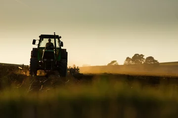 Crédence de cuisine en verre imprimé Tracteur Tracteur au coucher du soleil labourant le champ