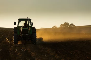 Crédence de cuisine en verre imprimé Tracteur Tracteur au coucher du soleil labourant le champ