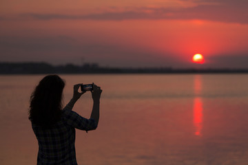 Silhouette of woman taking picture of sunset with a phone