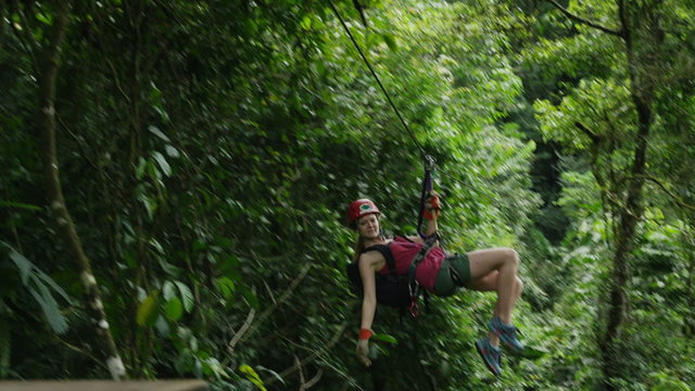 Medium low angle tracking shot of woman ziplining to landing in forest / Quepos, Puntarenas, Costa Rica