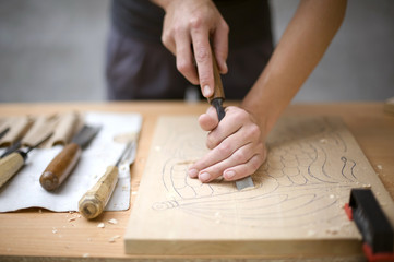 Artist carves a wooden plate with a chisel