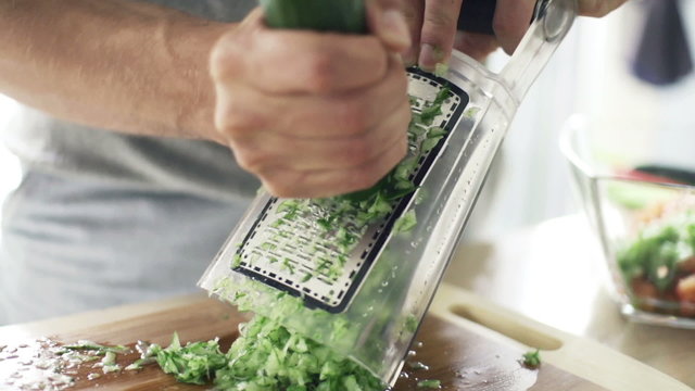 Man grating cucumber on grater in kitchen, slow motion 240fps
