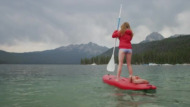 Wide shot of young woman paddleboarding on lake / Redfish Lake, Idaho, United States