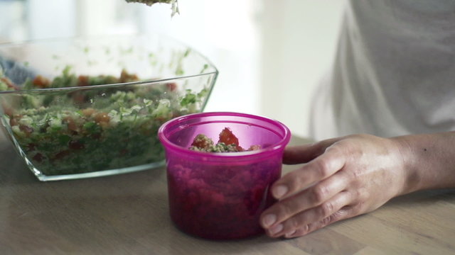 Woman putting salad into box in kitchen, slow motion 240fps
