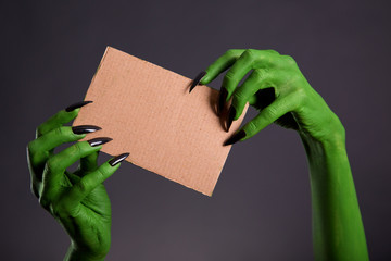 Green hands with long black nails holding empty piece of cardboa