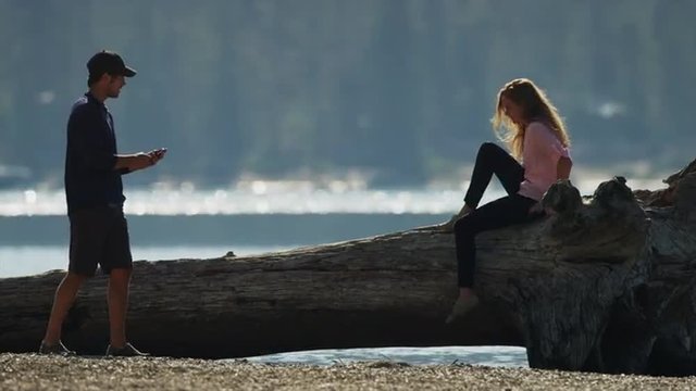 Medium shot of man photographing girlfriend on log at lake / Redfish Lake, Idaho, United States