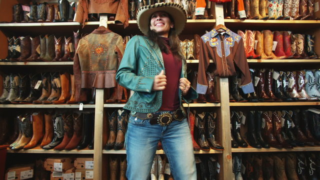 woman trying on a leather jacket and a cowboy hat at a western store
