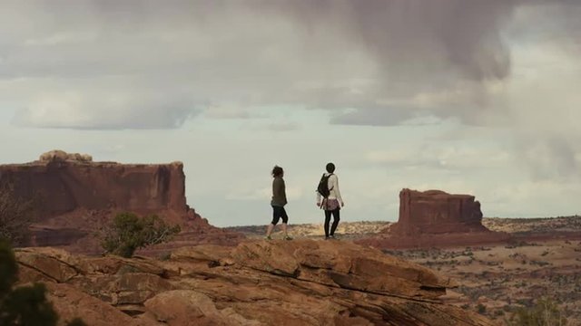 Wide shot of women standing on mountain with scenic view / Moab, Utah, United States