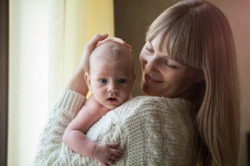Happy mother holding her baby at home by the window