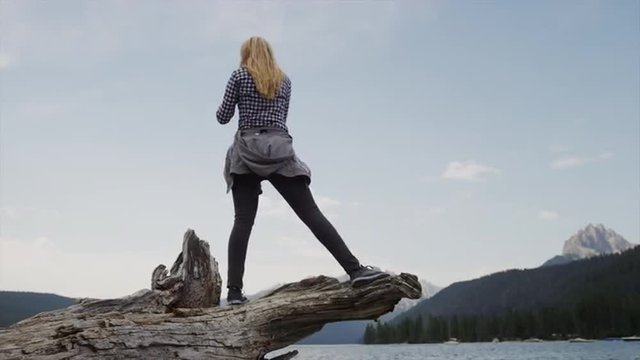 Medium shot of young woman videoing lake and mountains with cell phone / Redfish Lake, Idaho, United States