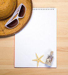 empty white notebook on wooden table surface with beach hat, sea